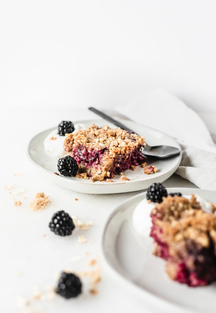 blackberry crumble baked oatmeal on a white plate with blackberries and a black fork. 