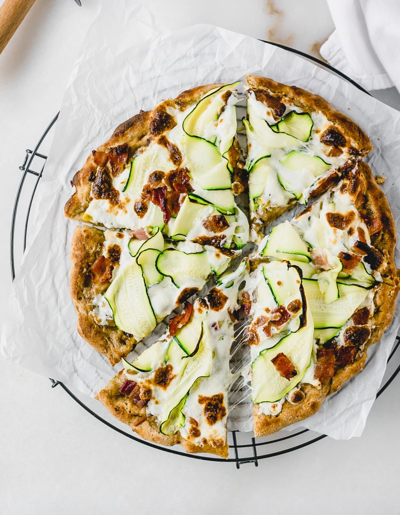 overhead view of zucchini bacon leek pizza on a parchment-lined wire rack.